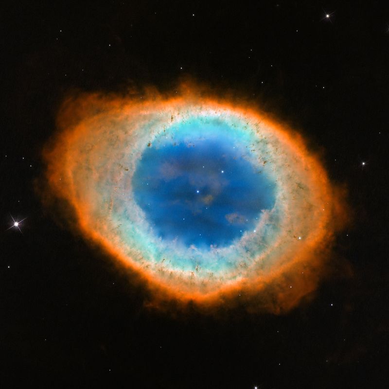 Ein ringförmiger Nebel mit blaugrünem Inneren und rotem Rand; genau im Zentrum ein einzelner schwacher Stern.